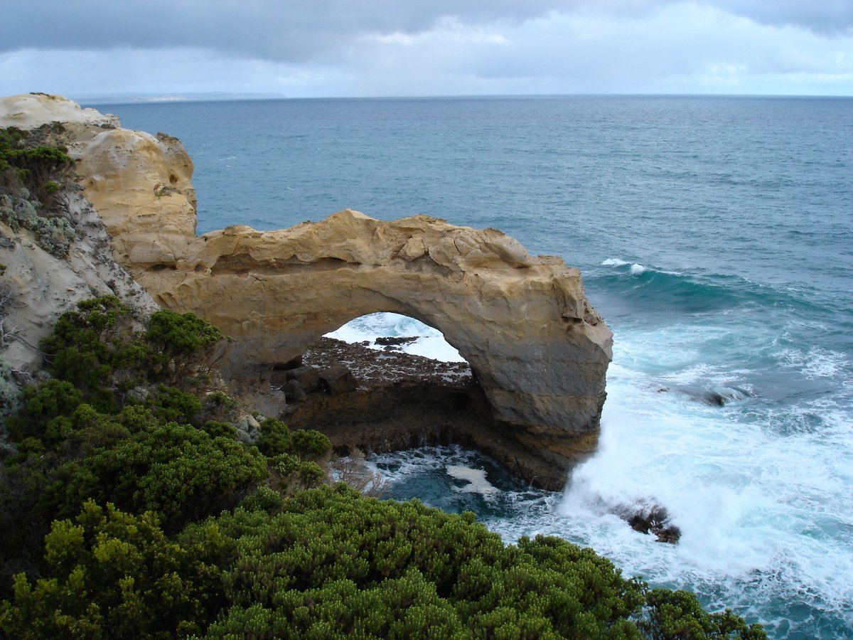 A natural limestone arch on the coast near Peterborough with surf breaking through beneath it under a moody sky