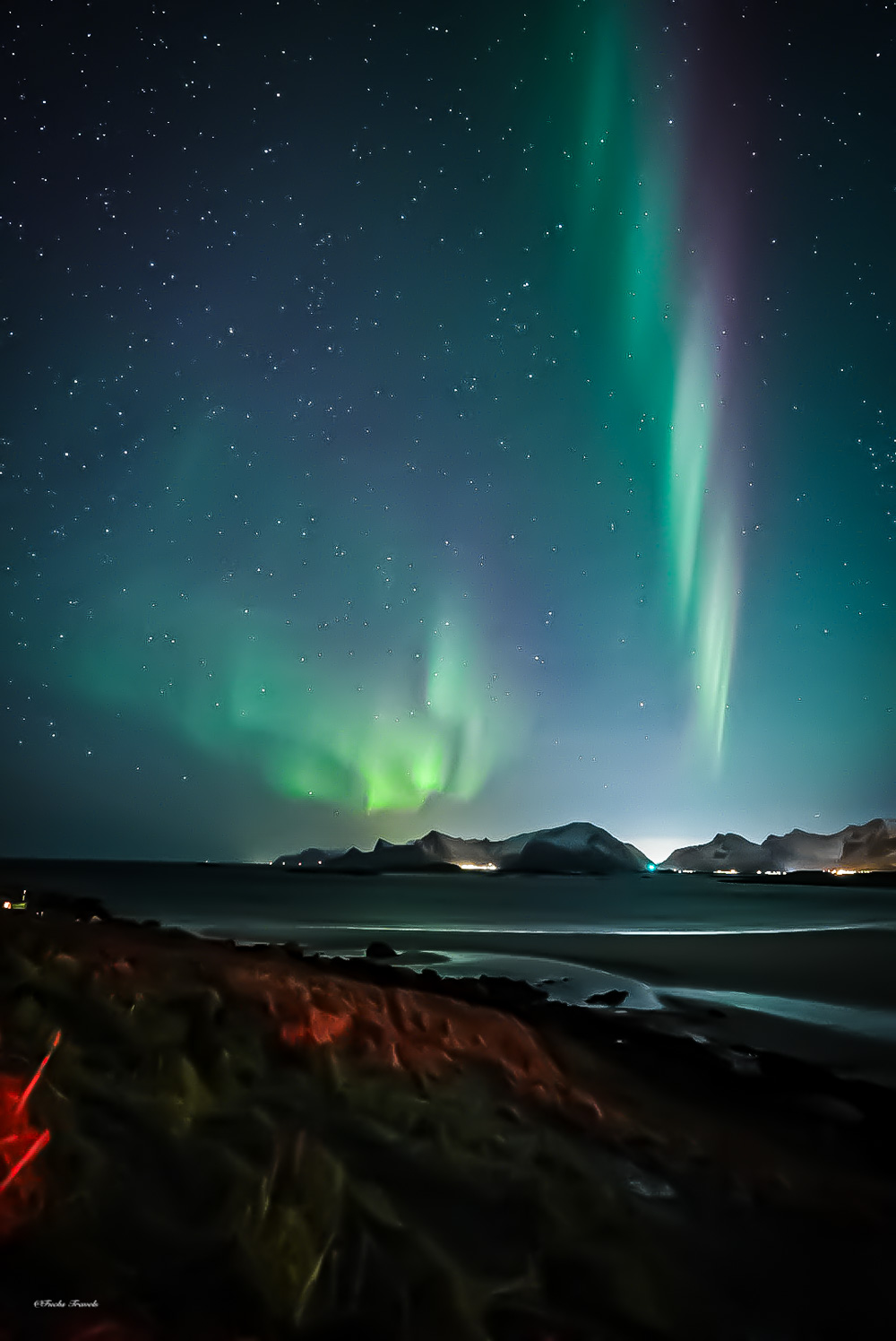 Vivid northern lights over a Lofoten beach at low tide with mountains on the horizon, Norway