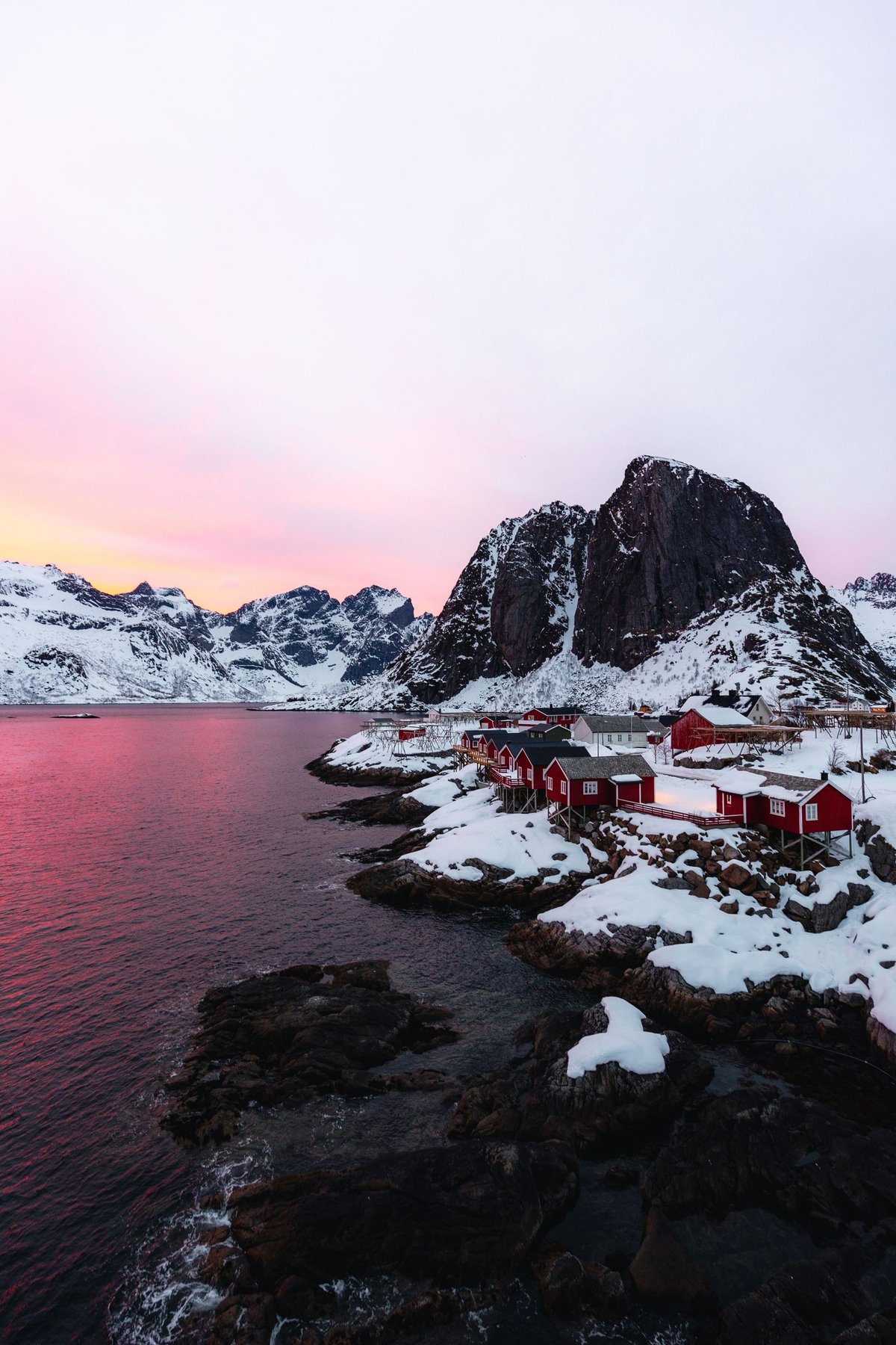 Red rorbuer fishing cabins at Hamnøy beneath Festhæltinden at winter dawn, Lofoten Norway